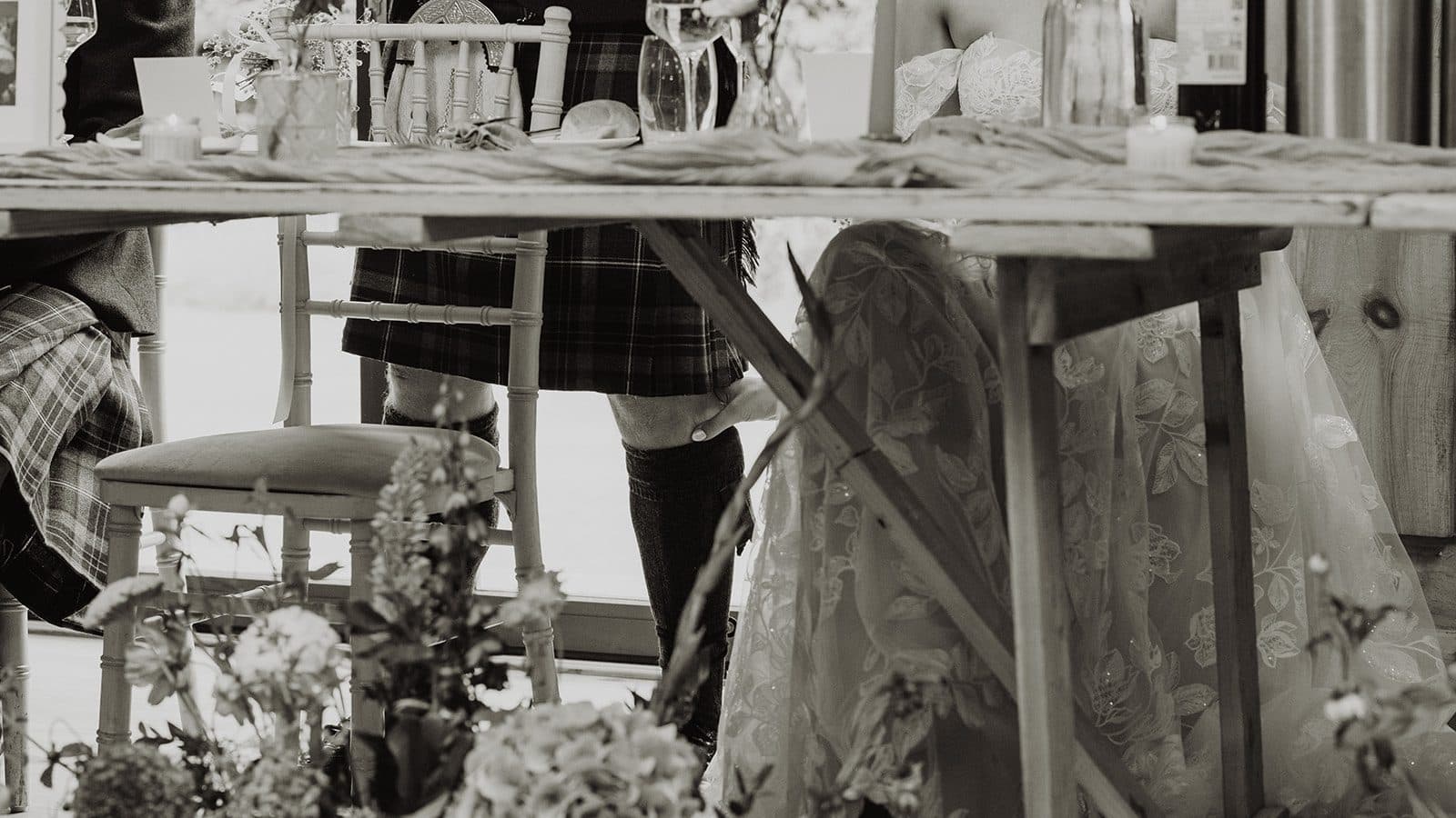 Under the top table during the speeches, the bride's hand rests on the groom's knee below his kilt